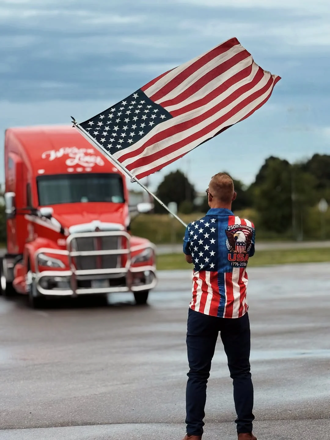 A Wilson Lines team member holding an American flag in front of a red truck.
